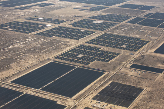 Aerial view of a geometric expanse of solar panels glinting under the desert sun, a mosaic of dark rectangles amidst the arid landscape, Boulder City, Nevada, United States.