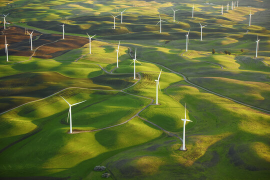 Aerial view of wind turbines standing tall on rolling green hills casting long shadows in the afternoon sun, Palouse, Washington, United States.