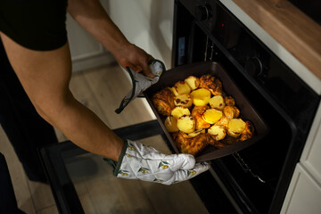 Man cooking dinner at his home kitchen, taking ready meal out of oven