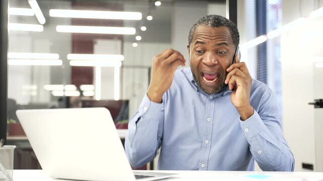 Angry dissatisfied african american businessman arguing talking on phone sitting in business office. Excited nervous manager emotionally talks with subordinate about problems that need to be solved