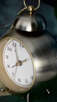 A moody, atmospheric close-up of a vintage-style metallic analog alarm clock resting on a stack of old books in dim light. The vertical, high-contrast scene evokes concepts of history, learning, time 