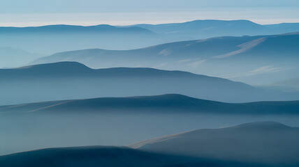 Serene mountain landscape showing layers of rolling hills fading into the blue mist and fog creating a minimalist and tranquil background with atmospheric depth