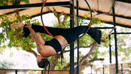Woman performing acrobatics on an aerial hoop, hanging upside down, demonstrating strength and...