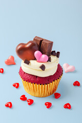 Valentines day red cupcake decorated with heart chocolate and pink hearts on blue background, celebrating love concept