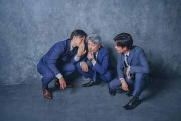 座り込んで噂話をするスーツ姿のビジネスマン3人