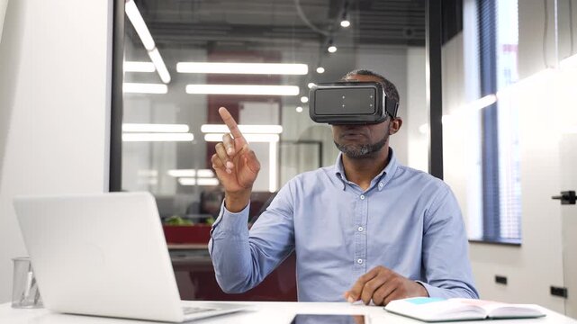African american businessman works using VR glasses in virtual reality simulator sitting in business office. Black man worker uses gestures to control computer programs and flips through virtual pages