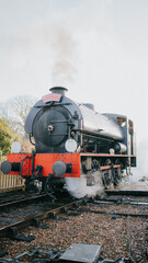 Obraz premium A steam train is on the tracks, with smoke coming out of the engine. The train is old and has a red and black design