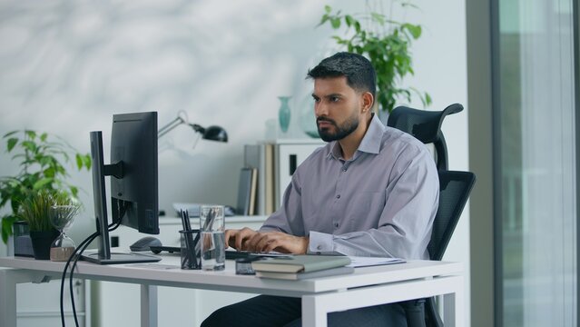 Arabian business man working with computer in office serious typing keyboard chatting with client Muslim businessman Indian boss leader work online looking at screen indoors busy developing project