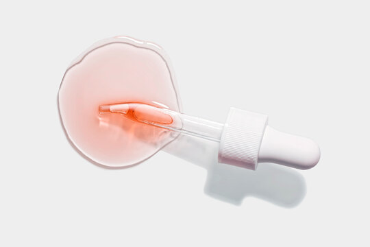 Liquid pink red orange oil or gel with pipette dropper or serum on white background