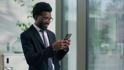 African American businessman smiling looking at smartphone in modern office happy male professional business man reading message using mobile phone digital communication success corporate workplace