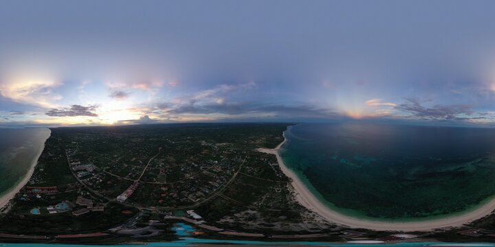 Aerial view of where the turquoise ocean kisses the sandy beach, framed by lush greenery under a sky streaked with dawn's pastel hues, Mombasa, Kenya.