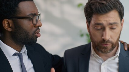 Two diversity multiethnic business men colleagues in office talking sad about problem work failure Caucasian upset man African American male support calming console multiracial businessmen friendship