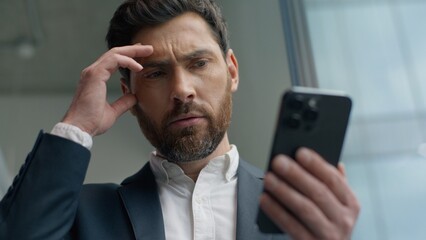 Shocked confused annoyed Caucasian male guy businessman business man in office looking smartphone reading bad news upset with mobile phone frustrated stressed failure app sad negative work problem