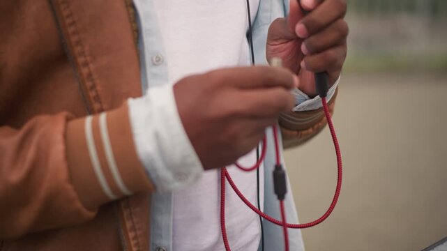 closeup hands threading red cable into jack and inspecting plug at outdoor mixer street dj adjusts cord and tests signal near controller, candid urban vibe with casual jacket and focused, energetic
