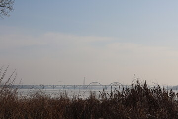Obraz premium View of a bridge over water surrounded by grass on a cloudy day with soft light in the sky
