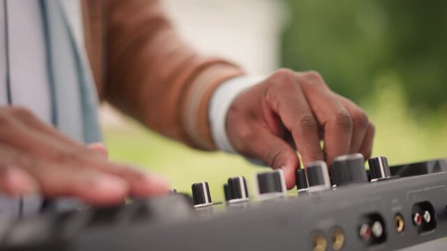 Hands finetuning audio equipment, Musician manipulating mixer dials during practice session outside, Disc jockey adjusting mixer settings and testing sound samples during outdoor rehearsal