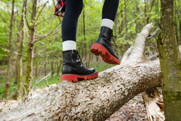 Close up of hiker's feet carefully stepping on fallen tree trunk while enjoying a leisurely walk through lush green forest, promoting concepts of adventure, exploration, and connection with nature