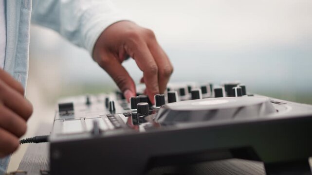 dj hands on controller outdoor set openair performance, swift fader moves and jog adjustments, crowdready transitions, visible cables and gear, denim sleeve, bright sky, rhythmic flow