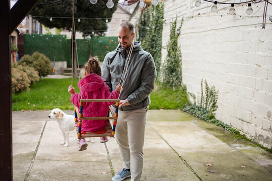 Father pushing daughter on swing in backyard with dog