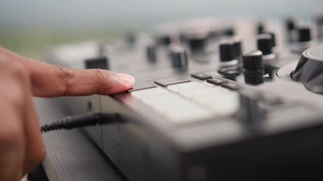Closeup pad controller black hand pressing pads outdoors on rooftop table portable drum machine with visible cable male black street musician taps pads and adjusts knobs under natural sunlight