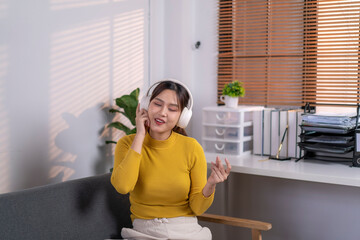 Asian freelancer woman enjoying music in headphones at home office