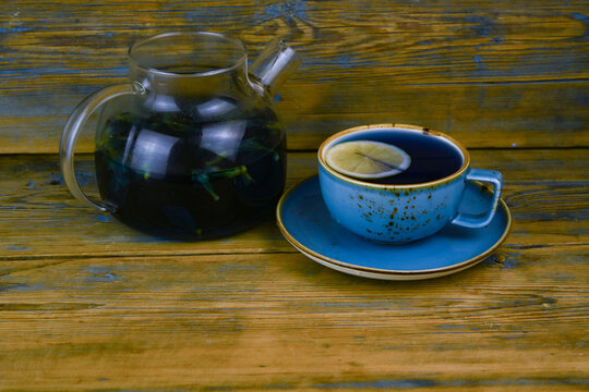 Refreshing blue  tea in cup and teapot on grey wooden table against gray background