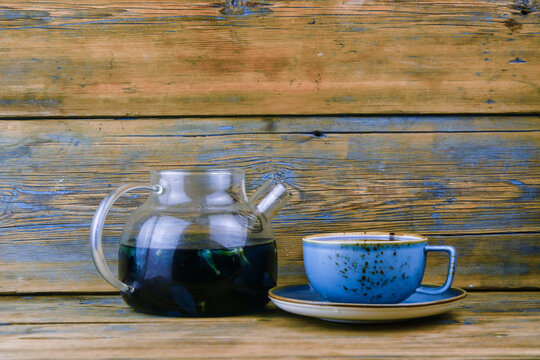 Refreshing blue  tea in cup and teapot on grey wooden table against gray background
