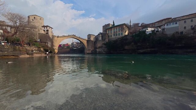 Low-angle time-lapse footage of large arched stone bridge spanning calm Neretva river under passing clouds Old bridge in Mostar, Bosnia and Herzegovina. UNESCO World Heritage site