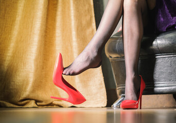 women's legs in black shiny tights and a red stiletto heel hanging from her toes