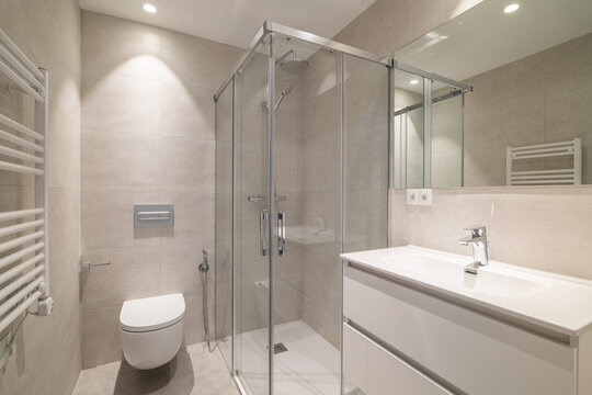 Modern bathroom with a glass shower, white sink, and toilet. Neutral color scheme with tiled walls and bright lighting.