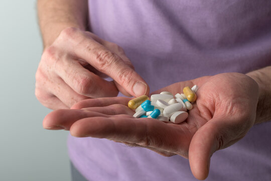 Adult male hand displays mixed pills and capsules while finger points at yellow capsule, concept medication choice and safety.