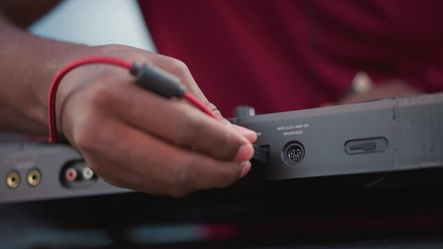 black DJ adjusting jack during soundcheck, tight closeups of fingers inserting red cable into DIN socket, quick patch swaps and channel checks, ambient crowd murmur and street set tension before drop