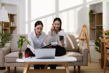 Two Asian women discussing a business project while working online from home. Lifestyle startup, remote work, teamwork, and small business collaboration concept.
