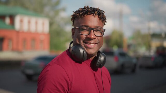 person with headphones on busy corner, medium shots capture smiling portrait against red brick building and green roof frames convey upbeat mood with DJ greeting neighbors, producer scouting samples,
