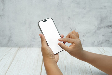 Two hands holding smartphone with blank white screen on bright wooden desk and light wall background. Concept of mobile mockup, app interaction, UI UX presentation, and digital marketing.
