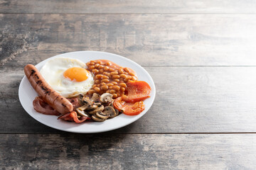 Full English breakfast with fried egg, bacon, sausages and beans on wooden table. Copy space