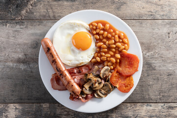 Full English breakfast with fried egg, bacon, sausages and beans on wooden table. Top view