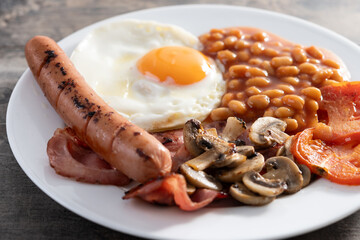 Full English breakfast with fried egg, bacon, sausages and beans on wooden table