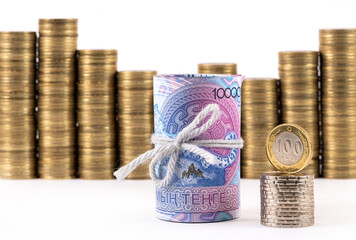 A conceptual story about the Kazakh financial system, featuring a stack of 10,000 tenge bills, 100 tenge coin and stacks of coins on a white background.