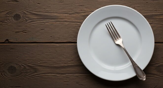 An empty white plate and fork resting on a rustic wooden table, representing a hunger, diet, or Lent fasting concept
