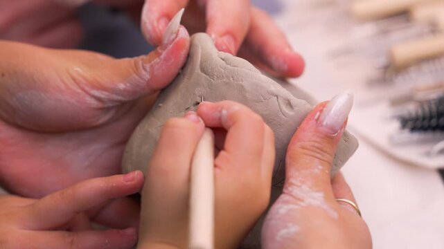 Crafting pottery on a wheel at a studio during a weekend workshop with hands shaping clay. A group of people work together to shape clay on a pottery wheel at a studio. Hands mold the wet clay into sm