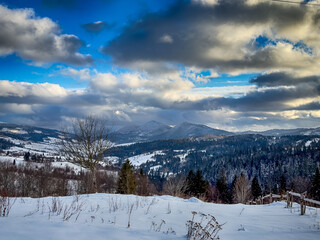 Mystical snowy Carpathian peaks under cloudy skies in the sunny weather