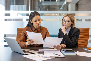Diverse businesswomen are collaborating on corporate documents during an important business meeting in a modern office, reviewing financial data and strategy together