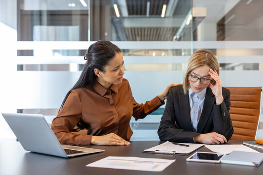 Businesswoman supporting and comforting a stressed colleague experiencing a headache and burnout, showcasing empathy and teamwork in a modern office environment