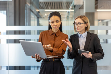 Two professional businesswomen collaborating and discussing a business project in a modern office....