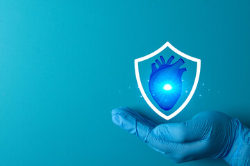 Heart health protection concept. Doctor hand in glove holding shield with cardiac organ symbol. Cardiology care, life insurance coverage, and medical safety on blue background with copyspace.