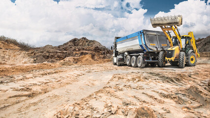 A loader loads sand and soil into a large dump truck at a construction site