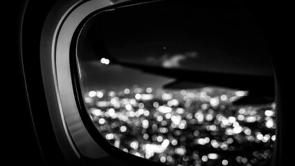 Nighttime city lights seen through an airplane window, with part of the wing in frame. Concept Night aerial city lights, Airplane window wing frame, Night flight photography, Window seat view