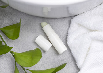 White blank cream tube near green leaves, basin and white bath towels on grey stone, mockup