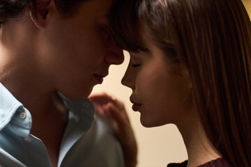 Fototapeta premium Young adult Caucasian man and young adult Caucasian woman standing close together touching foreheads with eyes closed showing intimate moment and gentle connection